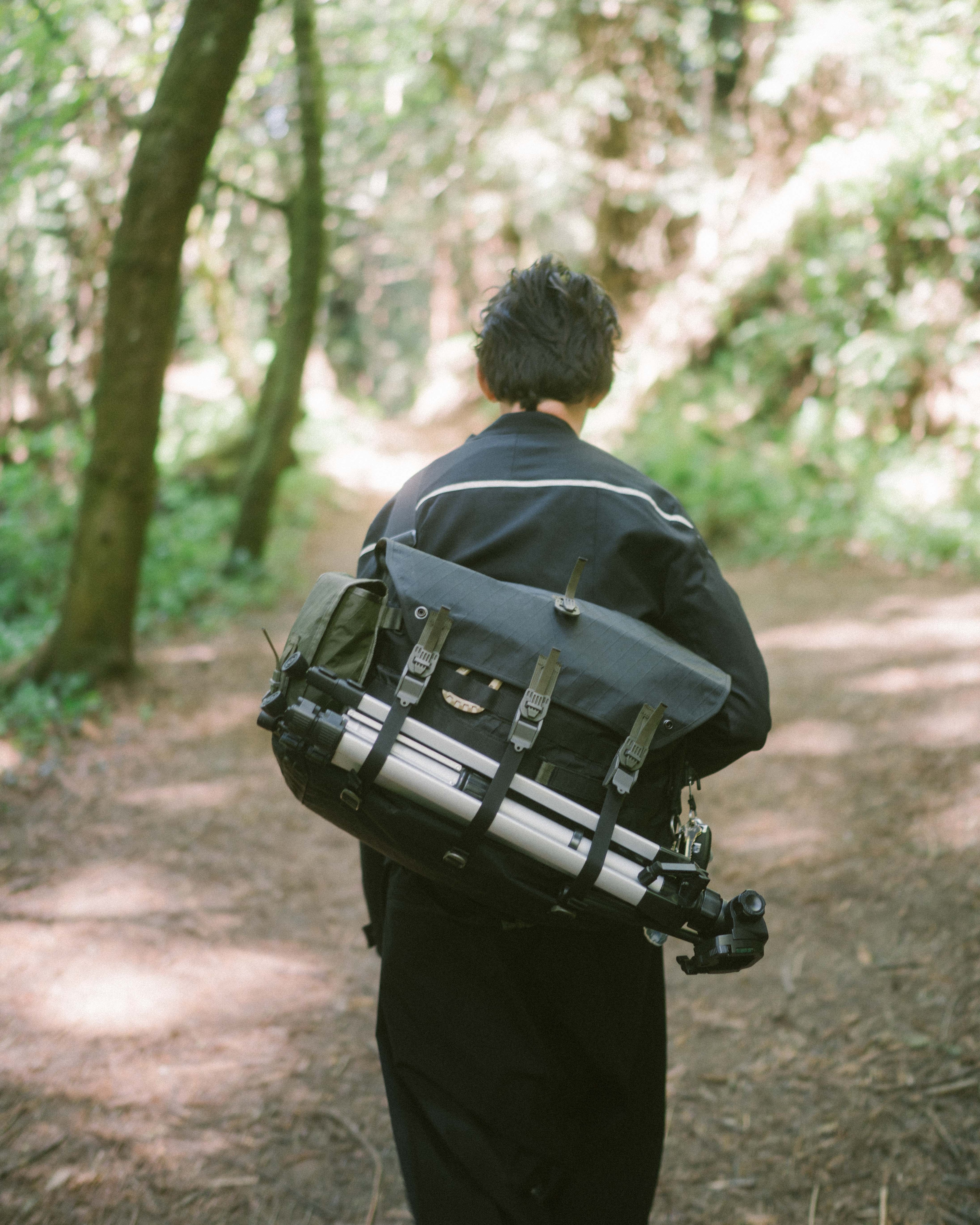 Matt walking into the forrest, with his tripod and camera gear hanging off the bag on his back.